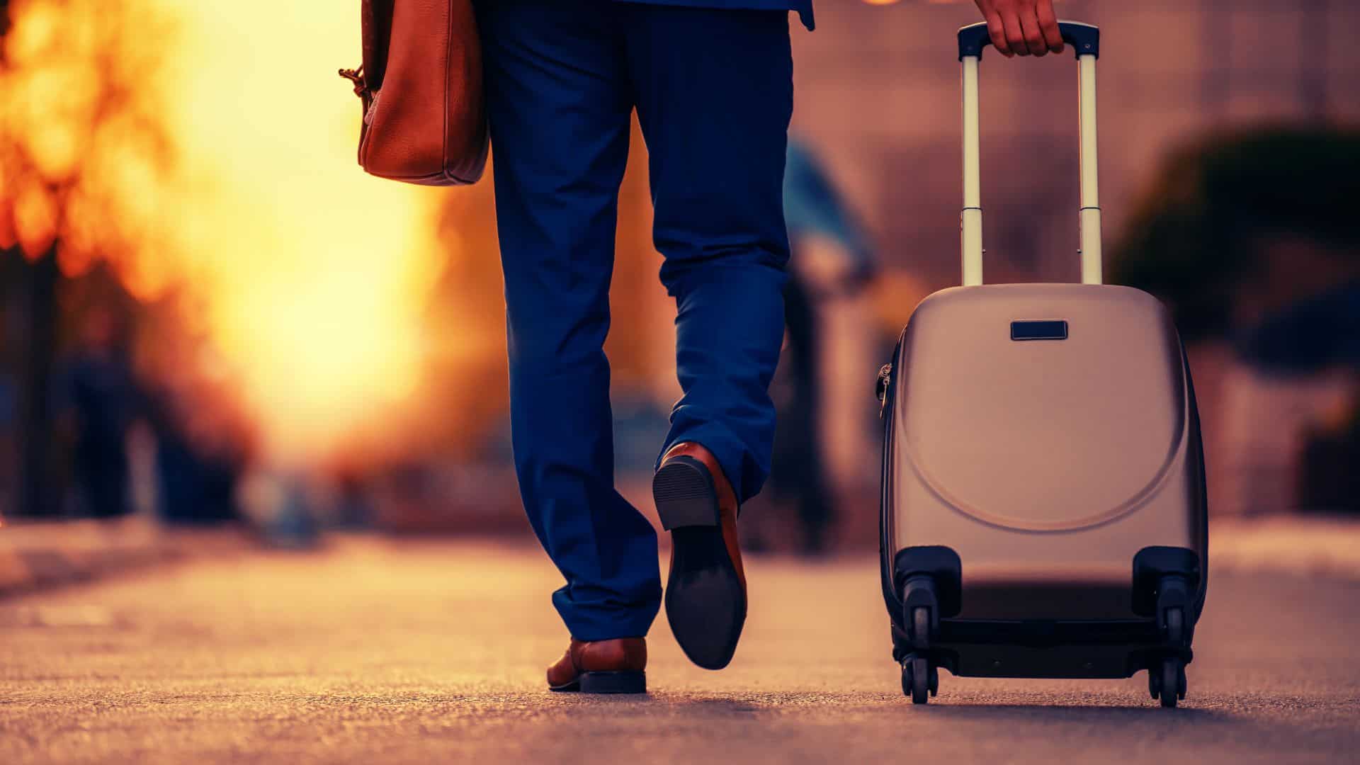 A businessman walking down the street with a wheeled suitcase.